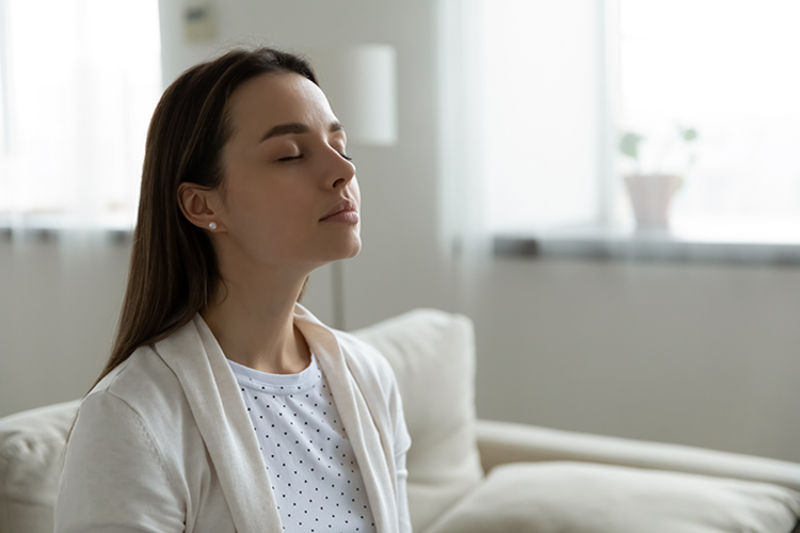Why Do I Need a Humidifier? A woman sitting on her couch enjoying clean air.
