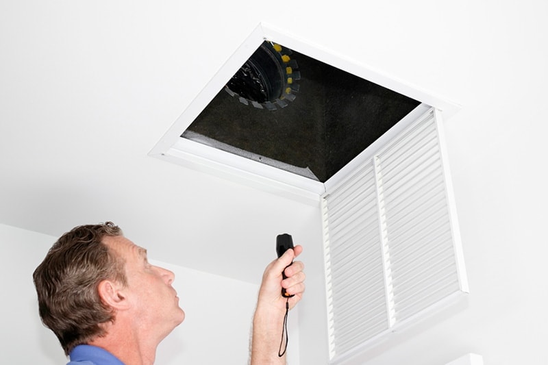 Man looking into an air vent with a flashlight.